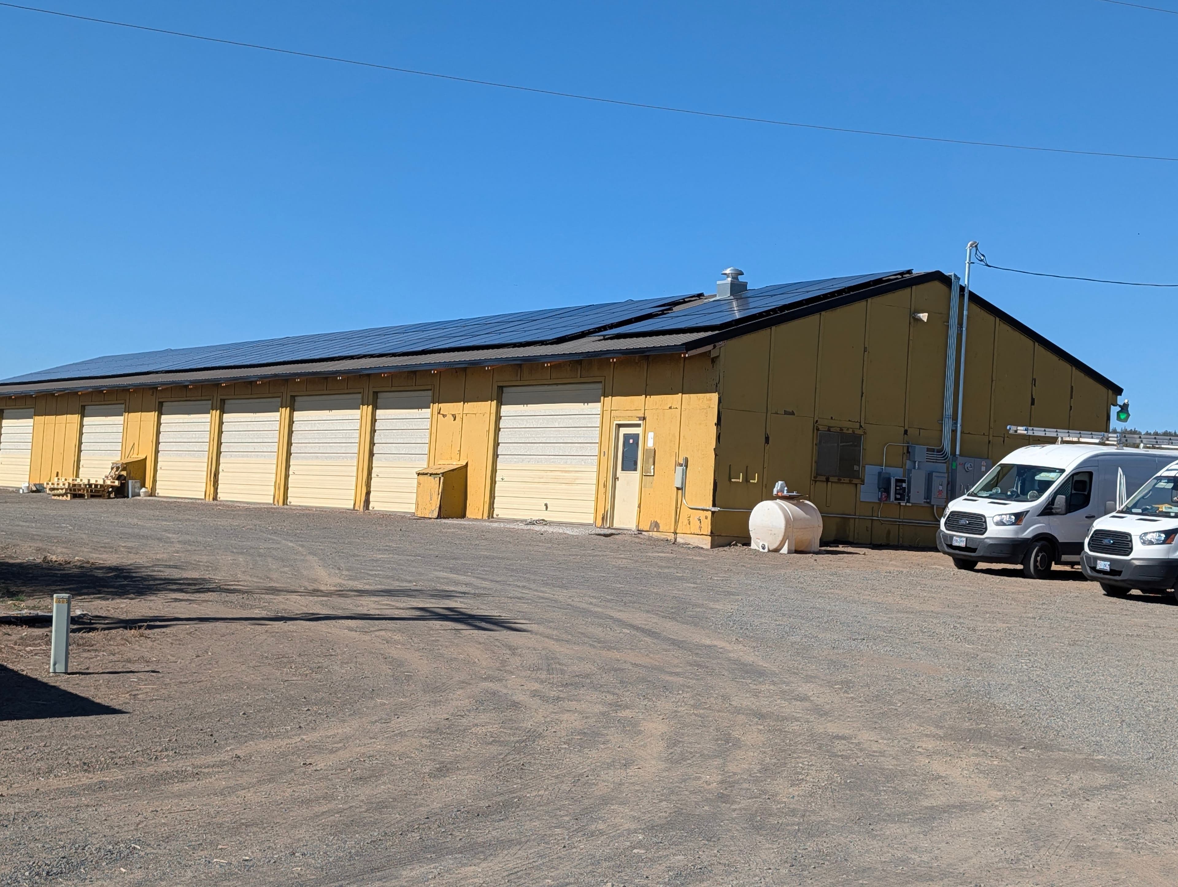 Large rooftop solar array on a yellow multi-bay shop building in Klamath County with National Solar vans parked outside.