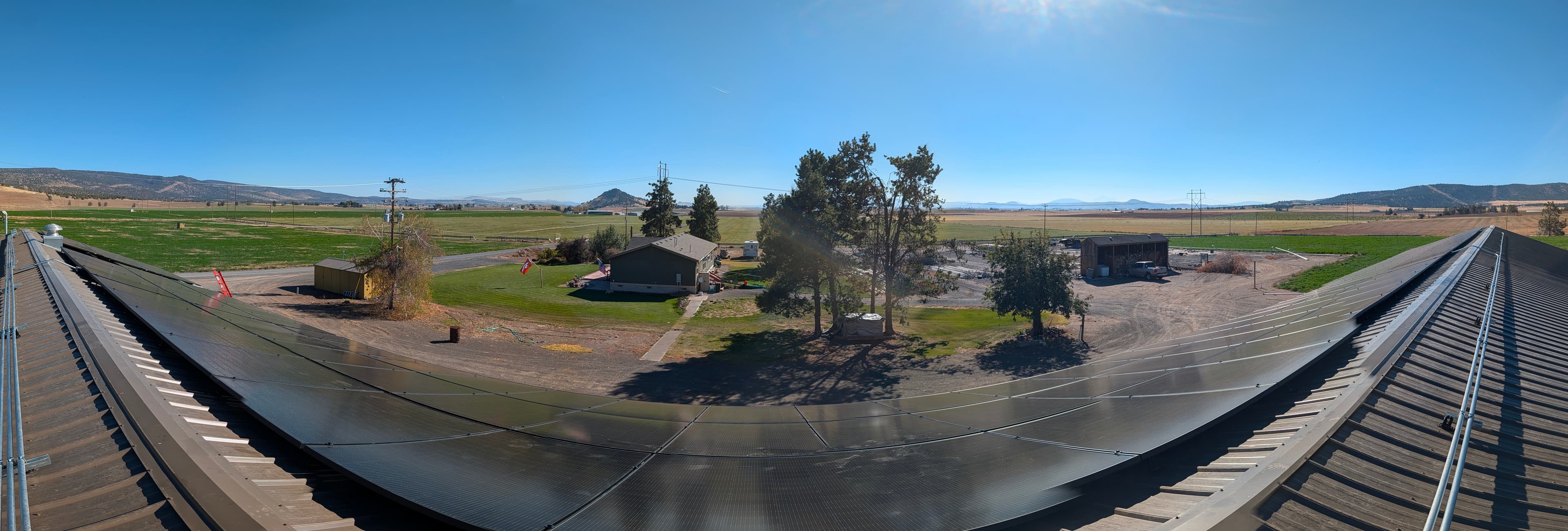 Panoramic view from the ridge of a metal shop roof covered in solar panels overlooking a Klamath County ranch.