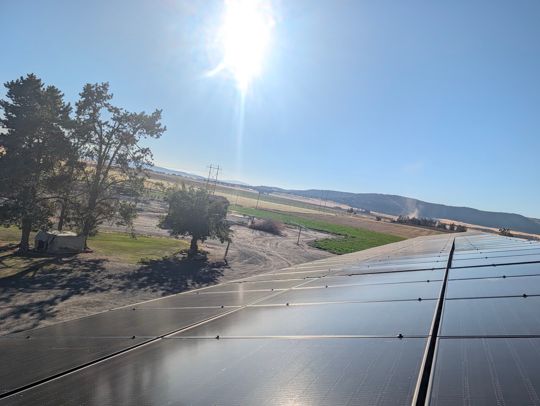 Sunlit rows of black solar panels on a Klamath County ranch building with fields and hills beyond.
