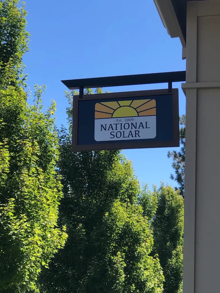 National Solar’s hanging sign outside the office, framed by leafy trees under a clear blue sky.