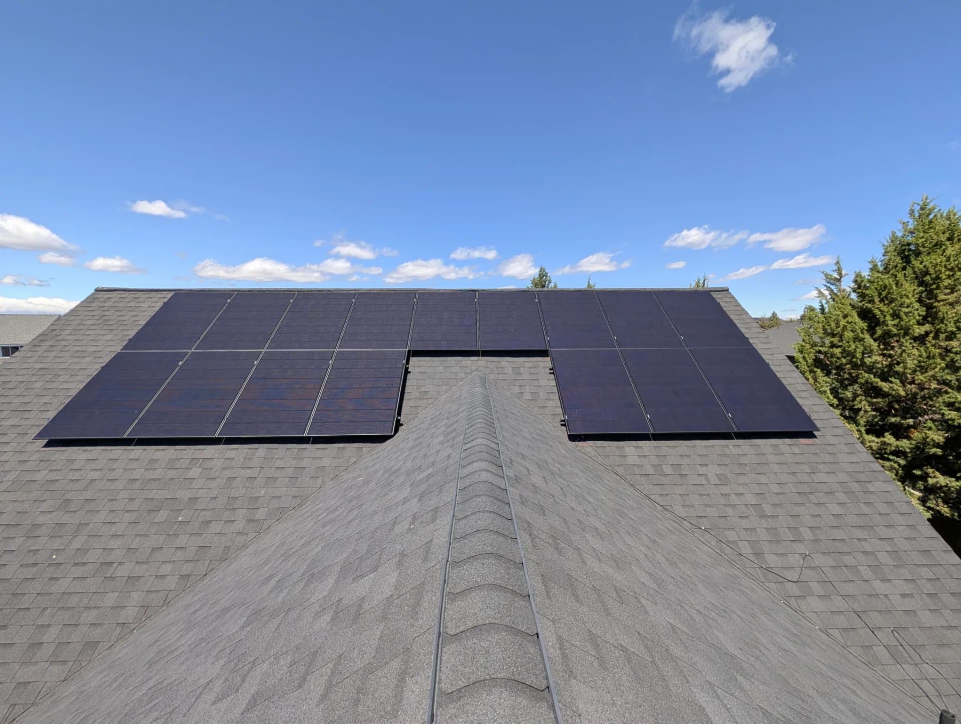 Rooftop solar panels mounted on both sides of a gray shingled ridge under a clear blue sky
