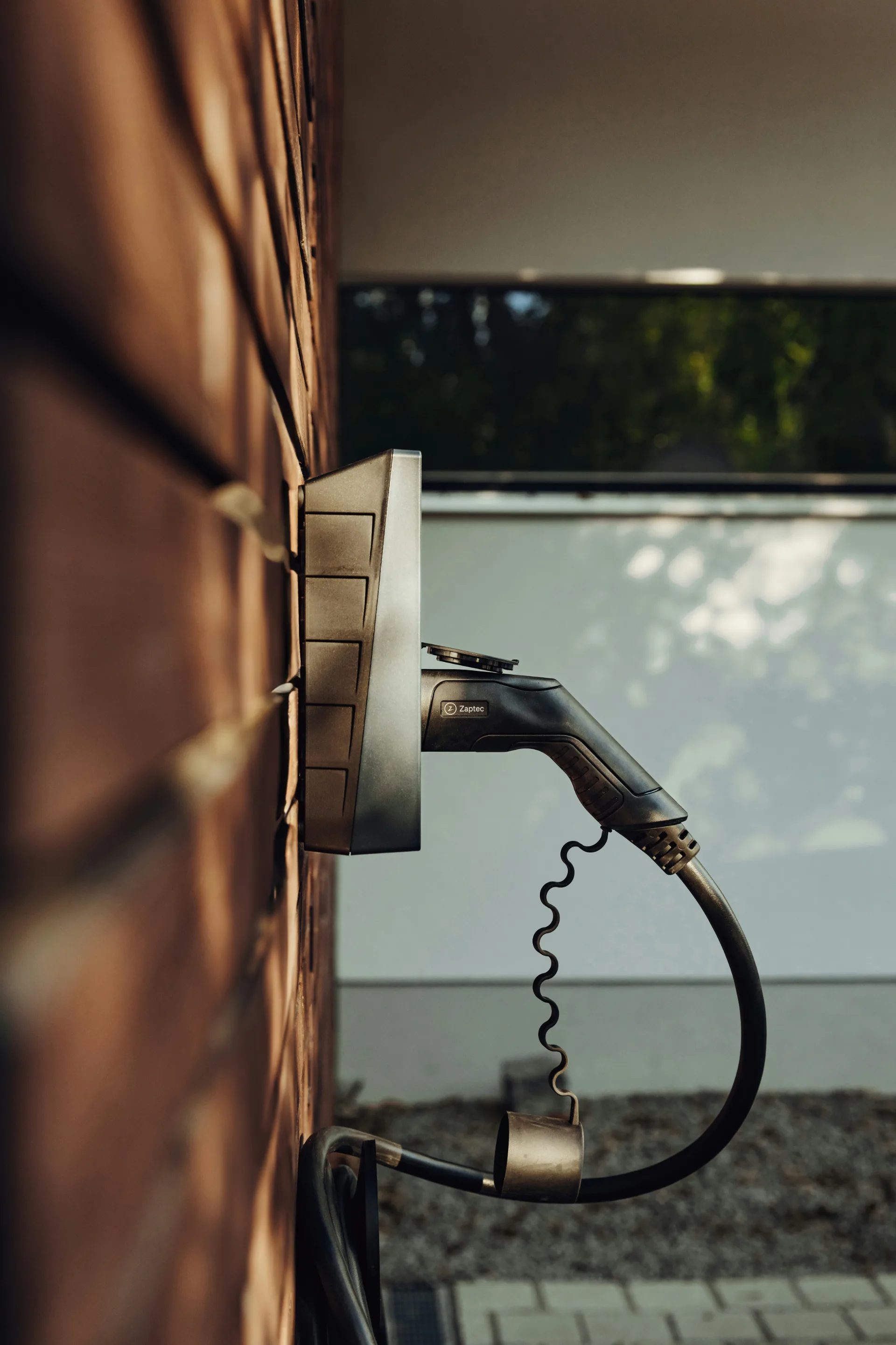 Wall-mounted electric vehicle charging plug and coiled cable attached to home exterior siding.